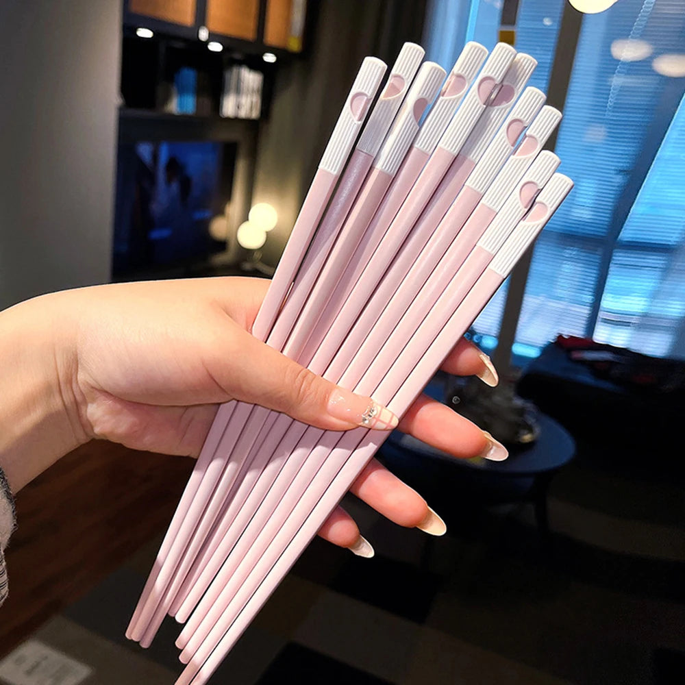 A hand holds a set of pink and white reusable Japanese Chinese chopsticks.