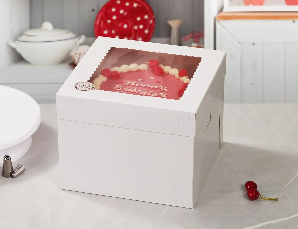 A white square window cake box with a pink and red design is displayed on a light surface.