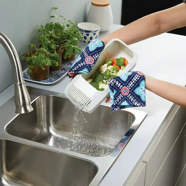 Eine Hand gießt Wasser in einen wiederverwendbaren Plastik-Nudelkocher, mit frischem Gemüse in der Nähe.
