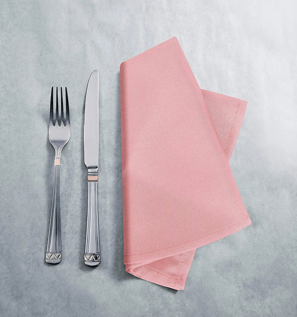 A set of silverware and a pink woven cloth napkin are displayed on a light gray surface.
