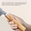 A hand holds a solid olive wood handle of an ergonomic Japanese style kitchen knife.