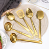 A set of golden stainless steel soup spoons and a colander displayed on a woven mat.