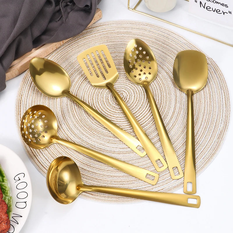 A set of golden stainless steel soup spoons and a colander displayed on a woven mat.