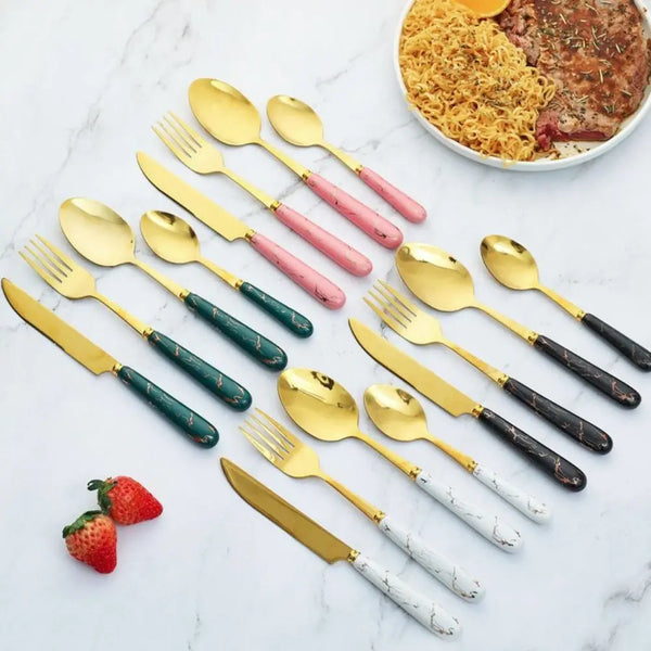 A 24-piece marbled stainless steel cutlery set with various colored spoons and forks arranged on a white marble surface.