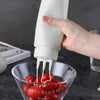 A hand squeezes a white dispenser bottle into a glass bowl filled with red tomatoes.