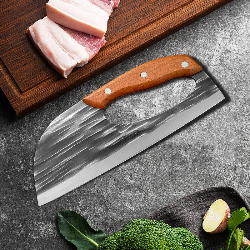 A hand forged boning knife with a wooden handle rests on a dark surface next to raw meat and vegetables.