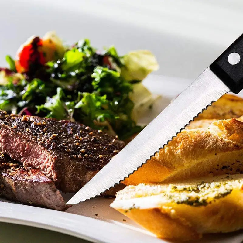A stainless steel steak knife is positioned next to a plate of grilled steak and a fresh salad.