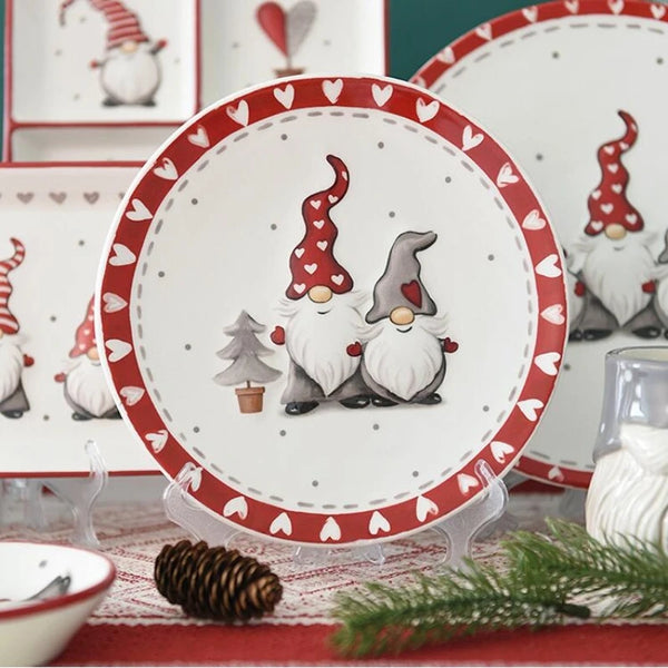 Weiße Keramikteller mit festlichem nordischem Weihnachtsmann-Design in Rot, auf rotem Stoff.