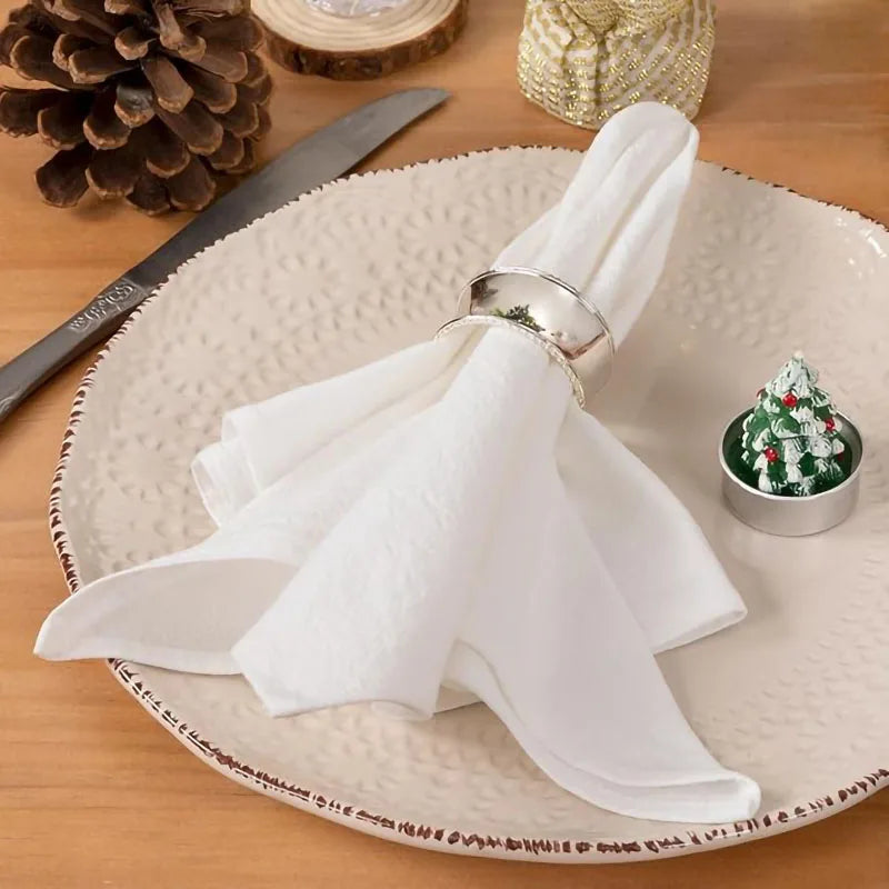 A set of white reusable cotton cloth napkins is neatly folded on a light-colored plate.
