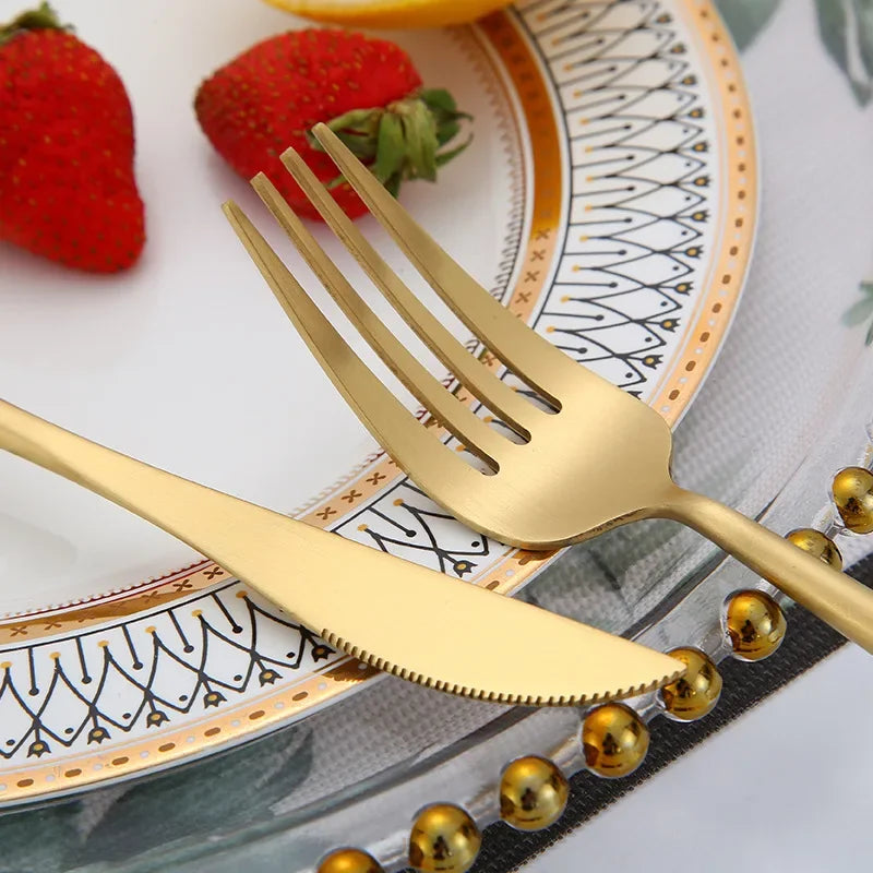A matte gold stainless steel fork resting on a decorative plate with strawberries and greenery.