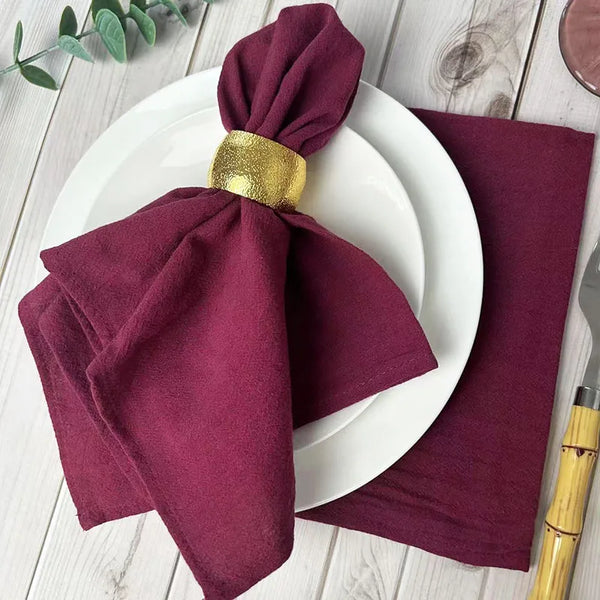 Ein Set aus sechs bordeauxroten Stoffservietten, gefaltet und auf einem weißen Teller und einer Serviette präsentiert.