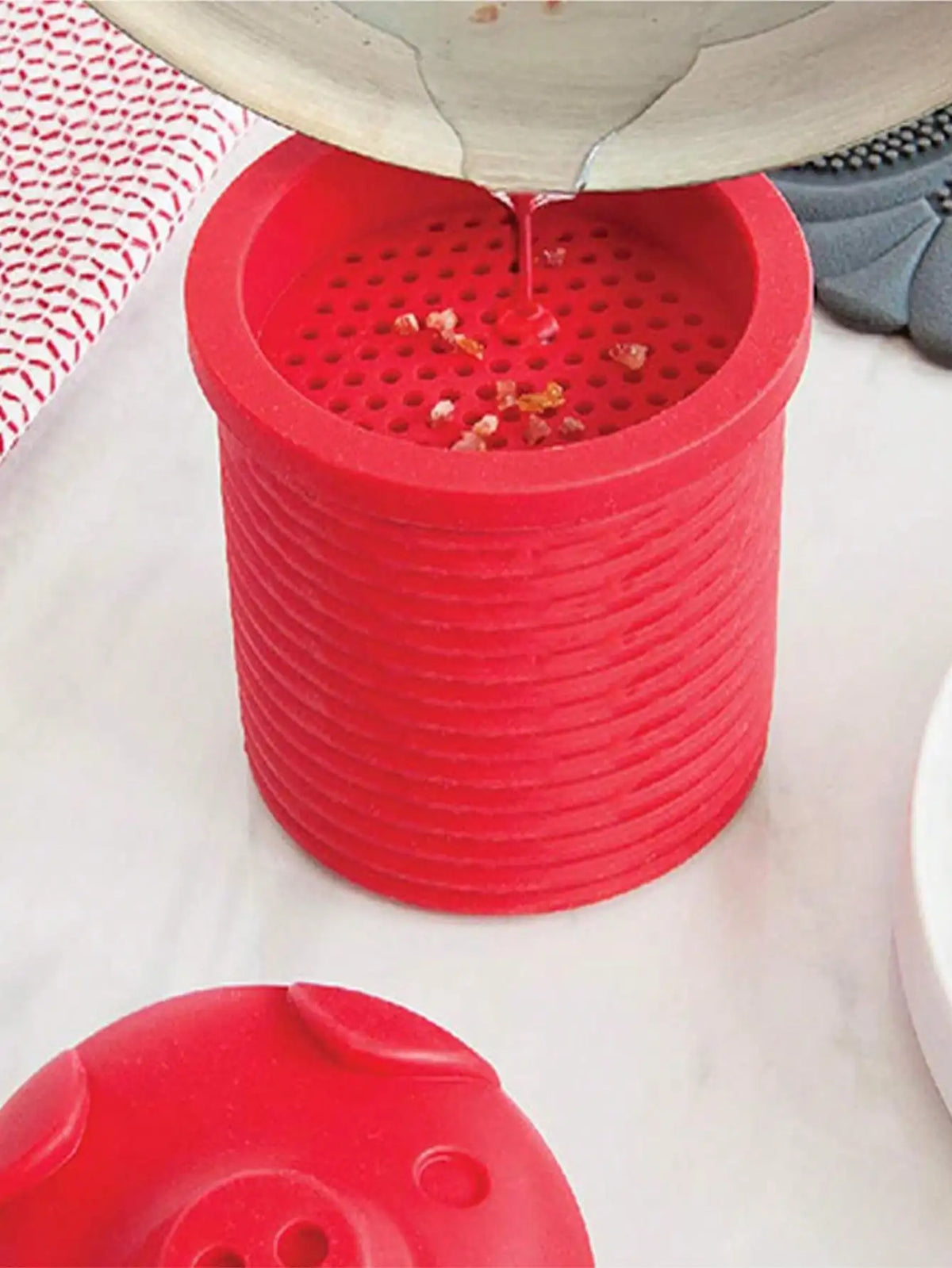 A red silicone grease collector is shown with oil dripping into it, resting on a white surface.