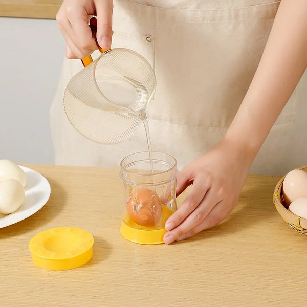 Eine Hand benutzt einen manuellen Schalenentferner, um ein Ei aus einem Glas zu entfernen. Ein Ei und ein gelbes Werkzeug lie
