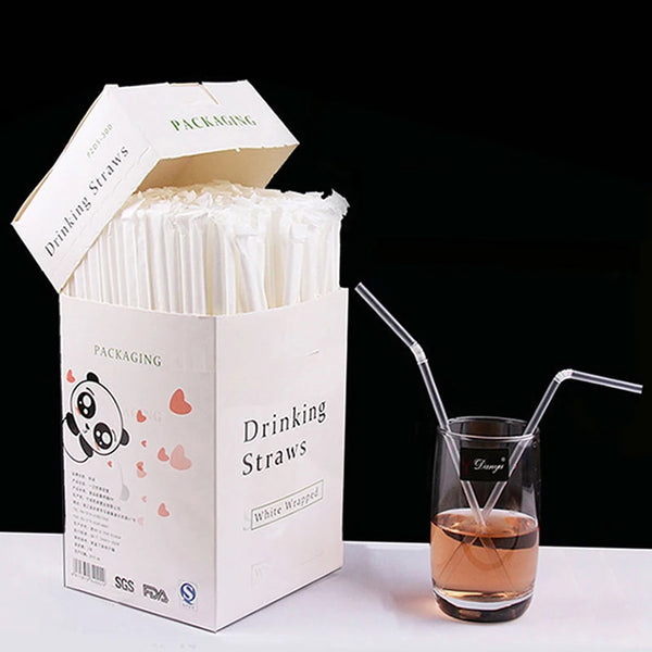 A box of individually wrapped clear plastic drinking straws is shown next to a glass of amber liquid.