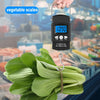 A hand holds a black digital hanging scale measuring a bunch of green leafy vegetables.