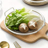 A stainless steel frying rack with an oil draining basket holding fresh lettuce and two round brown items on a wooden board.