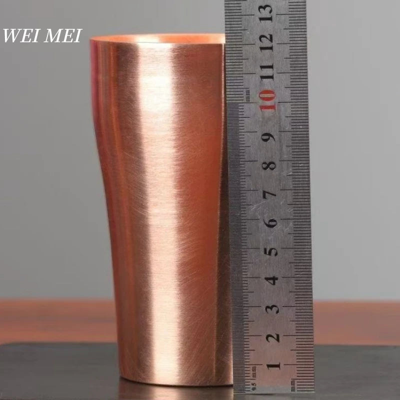 A handcrafted vintage copper coffee mug with a metallic rose gold finish shown next to a ruler.