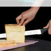 A hand is using a professional stainless steel bread and cake slicer knife to cut a slice of bread.