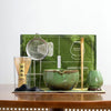 A traditional Japanese matcha tea set featuring a green bowl, whisk, and accessories displayed on a wooden surface.