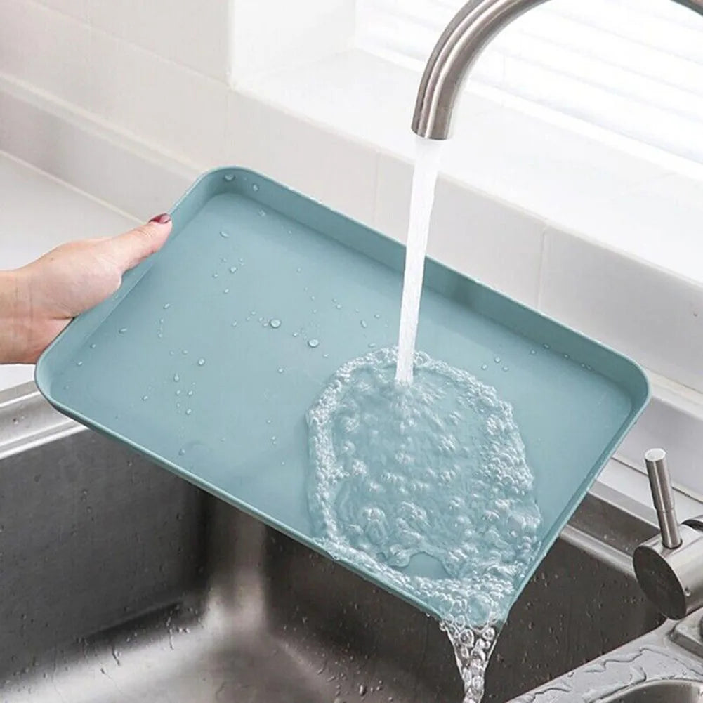 A rectangular serving tray is being filled with water from a faucet in a kitchen sink.
