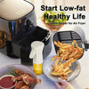 A hand holds a serving of golden french fries next to an air fryer and oil spray bottles.