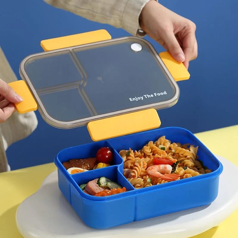 A hand places a clear, multi-compartment lunch box onto a blue bento container filled with food.