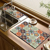 A rectangular rubber dish drying mat with a colorful floral pattern is placed on a kitchen countertop next to a stainless ste