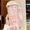 A pink insulated travel mug with cherry blossom floral design is held in a hand.