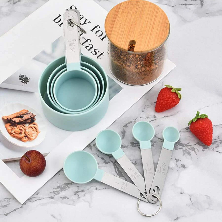A set of stainless steel measuring cups and spoons with a wooden lid displayed on a white marble surface.