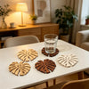 Ein Set aus fünf Holzscheiben mit tropischen Blättern als Untersetzer auf einem weißen Tisch.