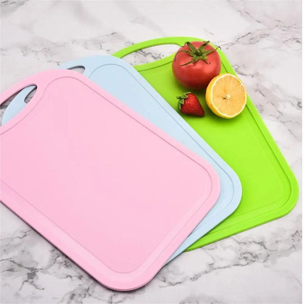 A pink non-slip plastic cutting board is shown next to a blue and green cutting board with fresh produce.