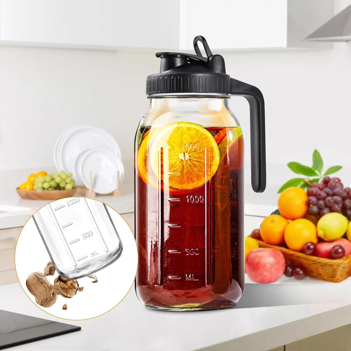 Botella de vidrio con asa negra llena de jugo rojo y rodajas de naranja sobre una encimera blanca.
