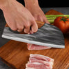 A hand is using a black and white hand forged boning knife to slice raw meat on a wooden cutting board.