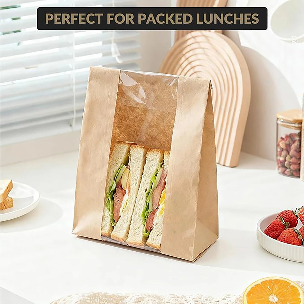 A brown kraft paper bakery bag with a clear window containing sliced sandwiches is shown on a white surface.