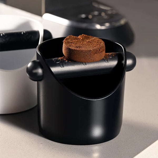 Schwarze, rutschfeste Kaffeeknallbox gefüllt mit Espresso-Mehl auf einer hellen Oberfläche.