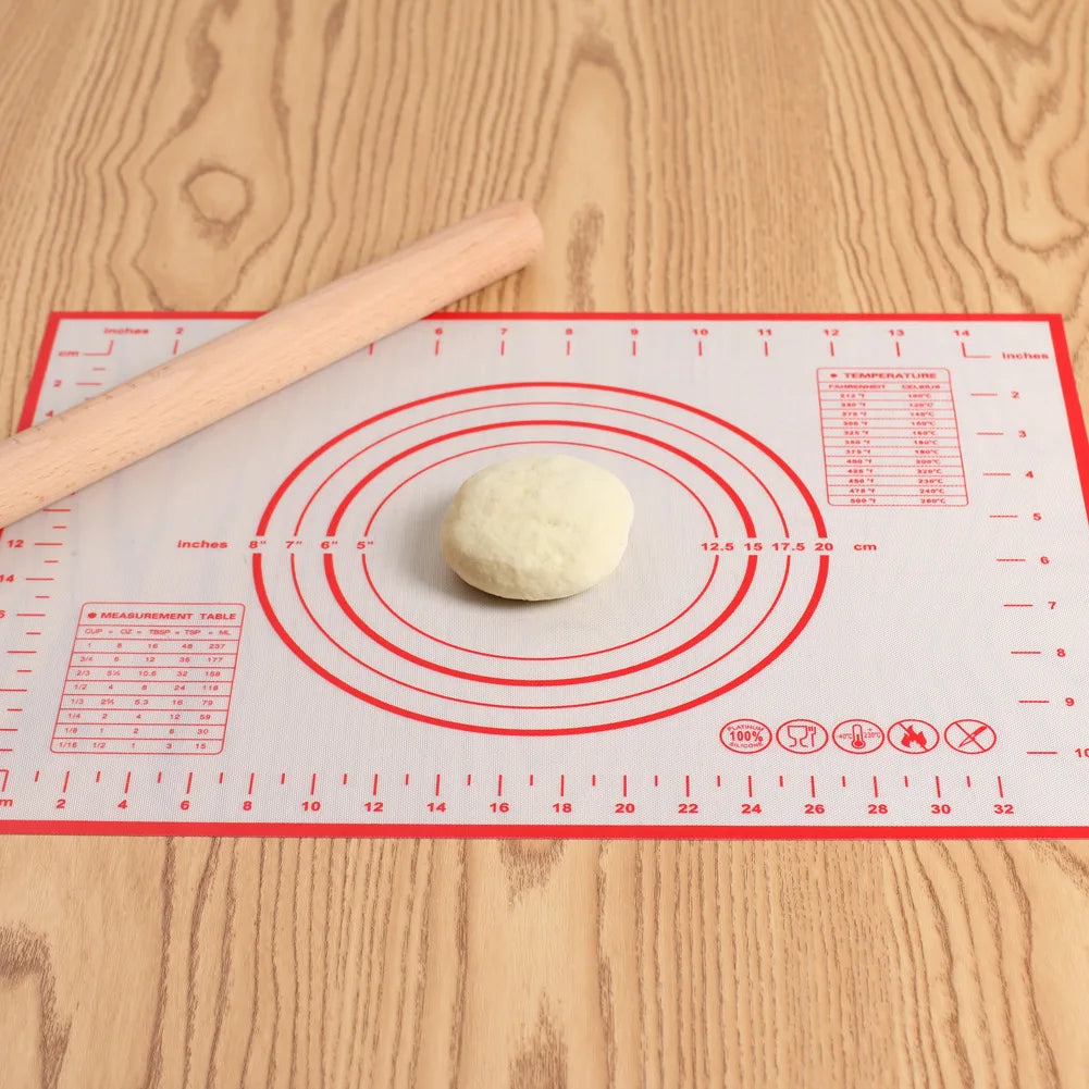 Ein runder Teigball liegt auf einer roten Silikon-Backmatte mit Messlinien und einem Holz-Nudelholz.