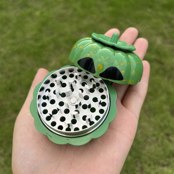 A hand holds a green pumpkin-shaped manual herb and spice grinder with an open lid.