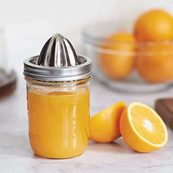 Edelstahl-Saftpresse mit Orangensaft in Glas und frischen Orangenscheiben