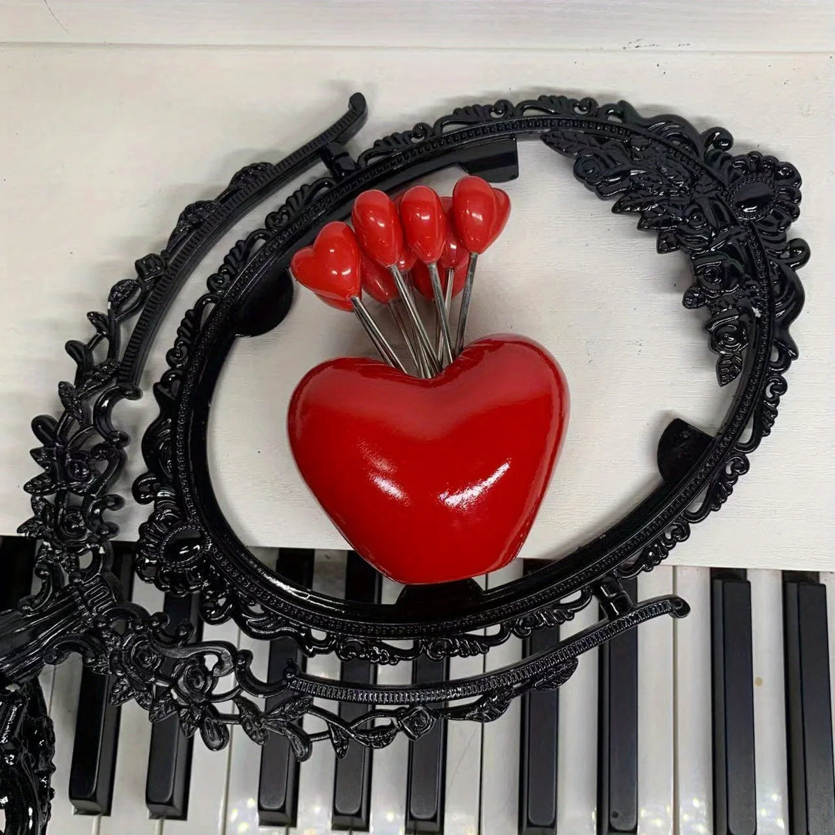 A red heart-shaped object is displayed within a black ornate wreath on a piano keyboard.