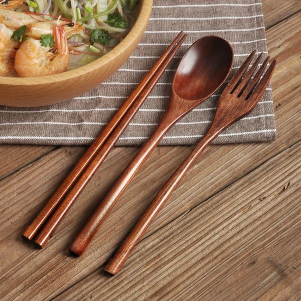 Set aus natürlichem Holzbesteck (Stäbchen, Löffel, Gabel) auf einem geflochtenen Servietten neben einer Schüssel mit Essen.