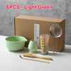 Seis utensilios de té de matcha verde claro, incluyendo cuencos y un batidor, junto a su caja de cartón.