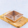 A square clear plastic food container with wooden base and measurements showing its dimensions.