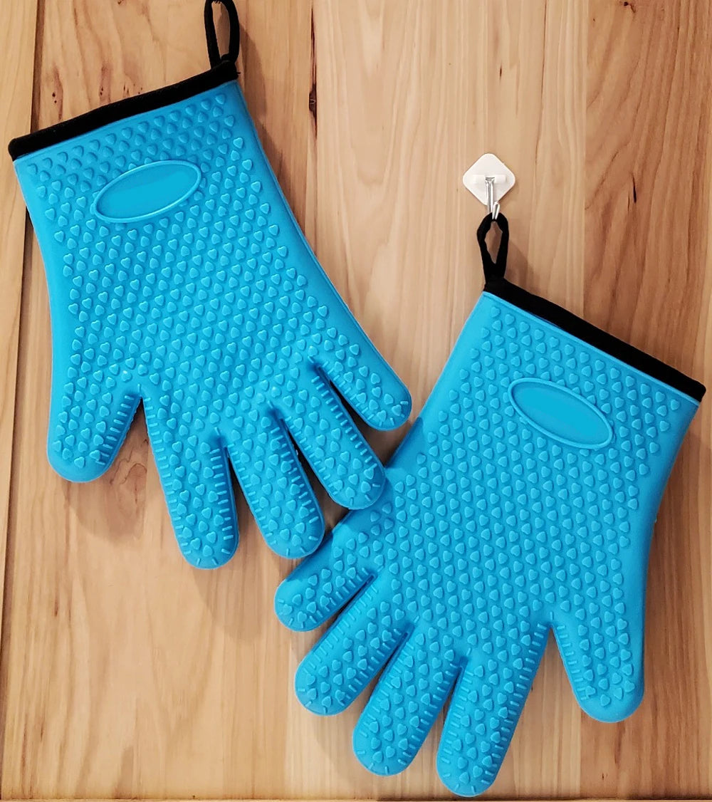 A pair of bright blue silicone oven gloves with a black strap hanging on a wooden surface.