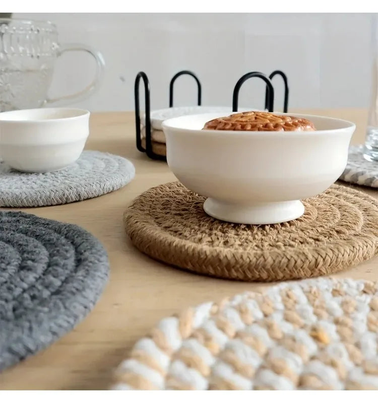 A set of four woven absorbent coasters displayed on a wooden table with white bowls and natural fiber mats.