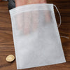 A clear plastic disposable non-woven tea filter bag is shown being held by a hand on a wooden surface.