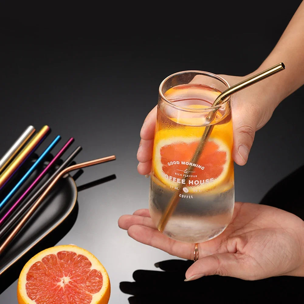 A hand holds a glass of iced tea with an orange slice and a metal straw against a dark background.