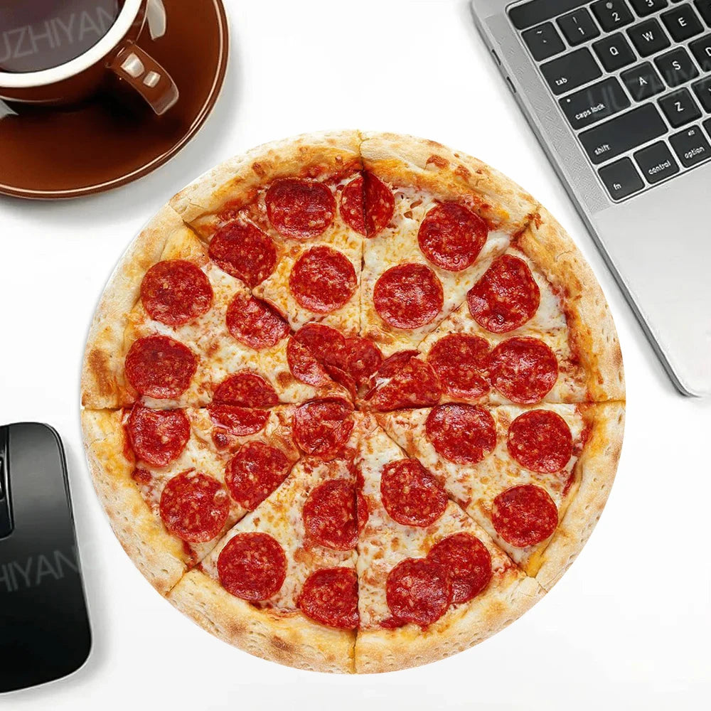 A round pizza cut into slices rests on a white surface next to a laptop and a black mouse pad.