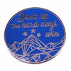 A blue enamel pin featuring the text Don't let the hard days win and a geometric mountain design.