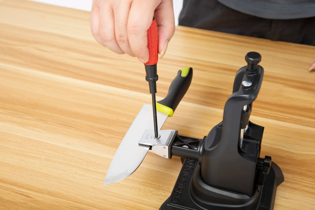 A hand is using a red tool to sharpen a diamond knife blade on a professional knife sharpener set.