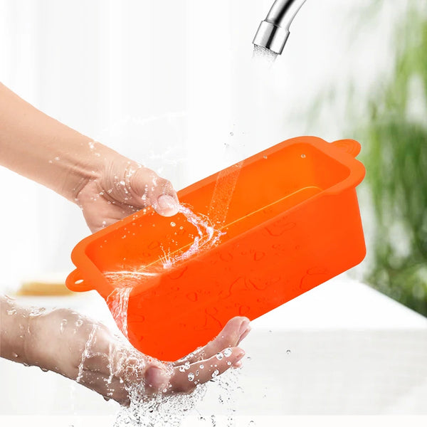 Hands are pouring oil into an orange silicone box for grilling.